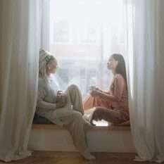 pexels-photo-6599085-6599085 Two women enjoying a morning chat by the window with steaming mugs, basking in sunlight.